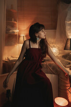 Peaceful Female In Red Dress Sitting In Cozy Room While Enjoying Evening And Looking Away