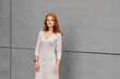 © Antonio Ovejero/ADDICTIVE STOCK - Positive young female with long red hair wearing casual dress and smart bracelet looking at camera while standing against concrete wall