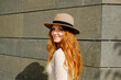 © Antonio Ovejero/ADDICTIVE STOCK - Side view of attractive positive young female with long red hair wearing stylish hat looking at camera while standing near stone urban building