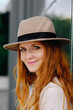 © Antonio Ovejero/ADDICTIVE STOCK - Side view of smiling young stylish ginger female in trendy hat while standing near modern building on city street
