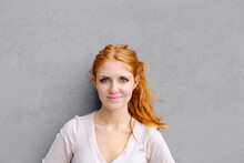 Positive Young Female With Long Red Hair Wearing Casual Dress And Looking At Camera While Standing Against Concrete Wall
