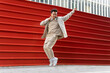 © David Munoz/ADDICTIVE STOCK - Full body joyful Asian male in casual wear listening to favorite song in wireless headphones while dancing along red metal fence