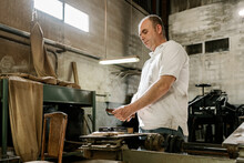 Low Angle Side View Of Concentrated Male Woodworker Creating Wooden Details While Standing In Grungy Garage At Daytime