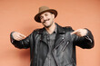 © joan corominas/ADDICTIVE STOCK - Trendy friendly male in hat and leather jacket smiling and looking at camera on beige background