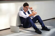© Luis Gomez/ADDICTIVE STOCK - From above of young masculine office worker in formal suit and eyewear sitting on floor near wall with cellphone and netbook