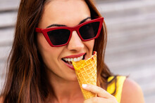 Delighted Young Long Haired Brunette With Red Sunglasses Enjoying Tasty Colorful Ice Cream In Waffle Cone In The Street In Summer Day