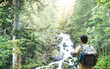 © Pol Sole/ADDICTIVE STOCK - Back view of unrecognizable man traveler with backpack standing on slope admiring amazing landscape of green forest with fast river