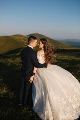 Groom and bride on the hill in mountains. Wedding couple in front of green hill. Newlyweds enjoying romantic moments in the mountains at sunset in beautiful summer day