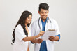 Indian young male and female doctor examining patient papers against white.