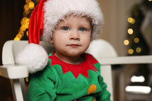 Baby In Cute Elf Costume Sitting On Chair At Home. Christmas Outfit