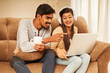 © krishna - Happy young couple using laptop at home on sofa.