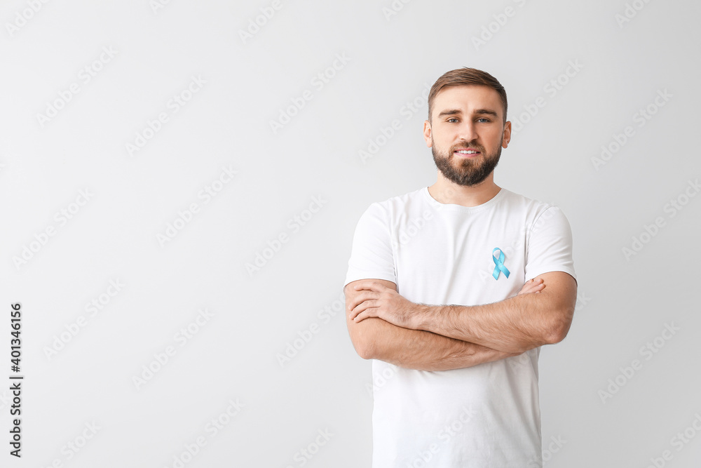 Man with blue ribbon on light background. Prostate cancer awareness concept