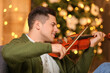 © Pixel-Shot - Young man playing violin at home on Christmas eve