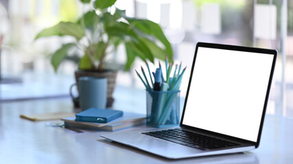 Wall Mural - Side view of an open laptop computer with white screen on creative designer workspace.