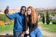 © Ladanifer - African black man and redhead caucasian woman smiling and taking a selfie with their smartphone in a park. Young multiracial couple portrait.