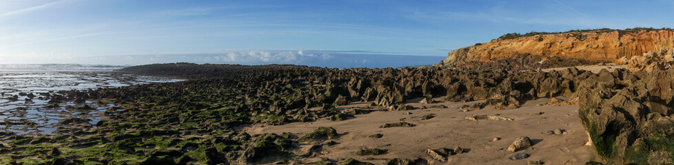 Wall Mural - panorama view of golden evening light reflectiing in tidal pools on a rocky beach with the ocean behind