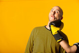 Fototapeta  - Middle aged man getting punched in the jaw. Hand of a man wearing boxing globes hitting other man in the face against a yellow background