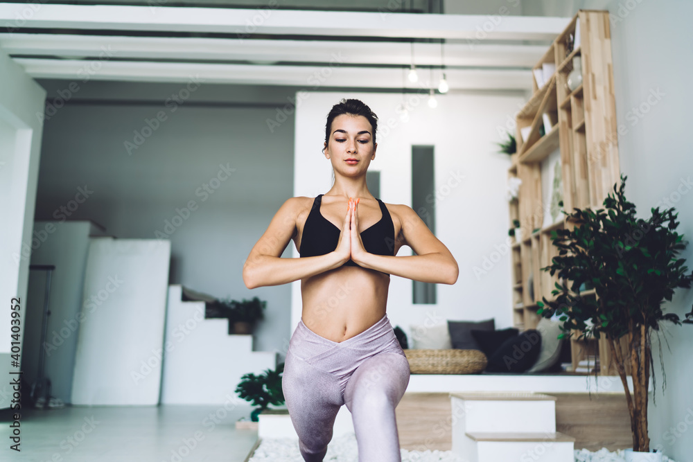 Perfect beautiful girl in comfortable tracksuit practicing stretching asana for training flexible muscles, attractive woman enjoying yoga workout training during morning time in home apartment - obrazy, fototapety, plakaty 