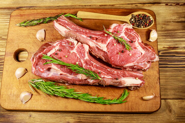 Wall Mural - Raw fresh beef rib eye steak on bone with spices, garlic and rosemary on wooden table. Top view