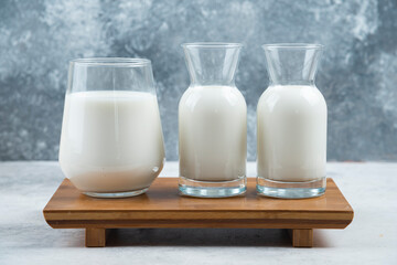 A glass cup of milk and two glasses jar of milk on a wooden small desk