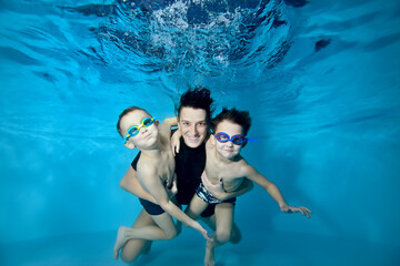 Wall Mural - Two little boys swim under the water with their mother. She hugs them tenderly. Active happy children. Healthy lifestyle. Swimming lessons under the water. Family sports