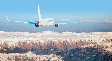 Wall Mural - Passenger airplane flying over snowy mountains - White passenger airplane rising over amazing clouds