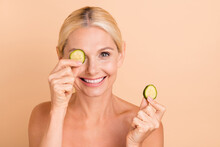 Close-up Portrait Of Lovely Blonde Cheerful Middle Aged Lady Closing Eye With Cucumber Slices Isolated Over Beige Pastel Color Background