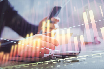 Double exposure of man's hands holding and using a phone and financial graph drawing. Analysis concept.