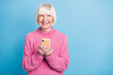 Photo portrait of old woman looking at blank space holding phone in two hands isolated on pastel blue colored background