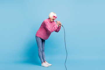 Sticker - Full length photo portrait of screaming old lady holding microphone in two hands isolated on pastel blue colored background