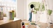 Young African American female alone painting wall with roller brush in olive color while renovating apartment. Rear of woman redecorating home, renovating and improving Repair and decorating concept