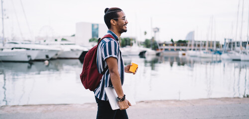 Side view of ethnic man commuting to work with coffee on quay