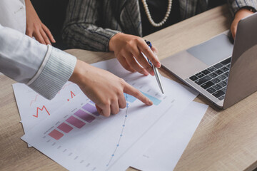 Cropped shot of two female workers discussing by pointing her index finger towards the chart sheet on the office desk