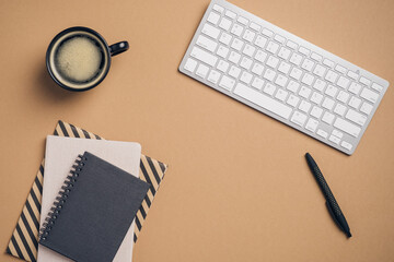 Poster - Flat lay, top view office desk with keyboard, cup of coffee, paper notepads, pen on brown background. Modern workplace concept