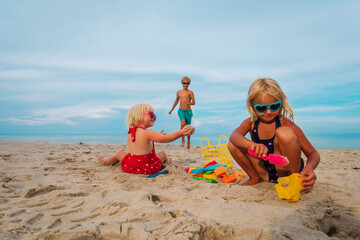 Poster - kids play with sand on beach vacation, boy and girls building sand castle