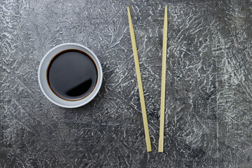 Wooden chopsticks, sushi sticks and saucepan with sauce on a gray background