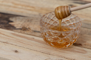 glass bowl with honey and honey dipper on a wooden table