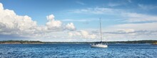 Small White Sloop Rigged Yacht Near The Rocky Finland Shoreline. Dramatic Sky. Transportation, Amateur Recreational Sailing, Sport, Cruise, Fishing, Leisure Activity. Panoramic View, Copy Space