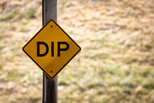 A Yellow Sign Signifying A Dip In The Road