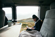 © BublikHaus - Young man sit inside customised camper van, work on laptop remotely from office, enjoys views while also stays connected. Millennial travel lifestyle. Work remote on the road
