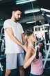 © themorningglory - Cheerful young woman wearing pink sports bra while doing chin-up exercise with trainer man