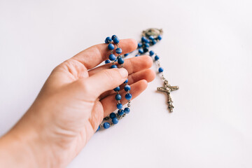 Blue beaded rosary held by a caucasian young woman's hand on white background.