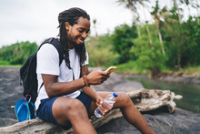 Smiling Black Man Using Smartphone In Tropical Forest Near River