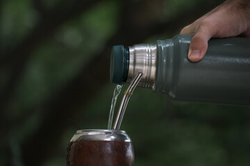 Poster - Selective focus shot of a hand pouring water from a thermos to a calabash mate cup with straw