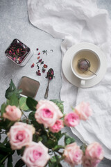 A vertical shot of a teacup with tea leaves, berry herbs in a jar decorated with roses on a table