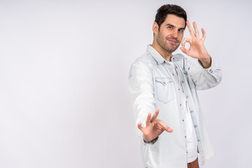 A young Caucasian male in a denim jacket doing okay hand gestures against a white backgrou