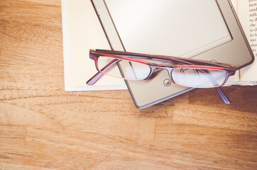 Poster - A tablet and book on a desk with glasses on top