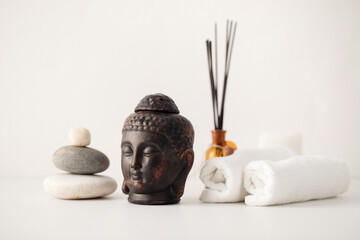 Clay buddha head aroma lamp, aroma sticks, stone composition and spa towels – spa composition on white background