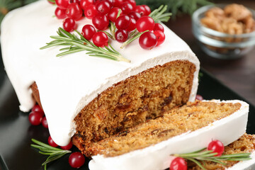 Traditional classic Christmas cake decorated with cranberries and rosemary on black plate, closeup