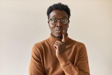 Wall Mural - Human emotions and body language. Portrait of funny cute young dark skinned guy in turtleneck sweater holding finger on his face, having pensive amazed facial expression, considering interesting idea